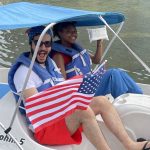 A photo of Twipes cofounders Al and Elle in a paddle boat holding up an American flag and a pack of Twipes to celebrate the company's expansion to America.