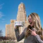 A photo of a woman pointing at a pack of Twipes truly flushable, truly biodegradable wet wipes in front of Buffalo City Hall