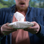 A photo of a man in front of trees holding a pack of Twipes with a look of awe on his face